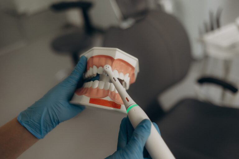 ADentistShowsHowToBrushYourTeethWithAn - Pascack Dental Arts Close-up of a dental model held by gloved hands while a dental tool is used near the teeth, illustrating a dental exam/teaching scene